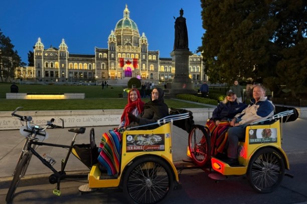 Four people in rickshaws in front of an illuminated building at night.
